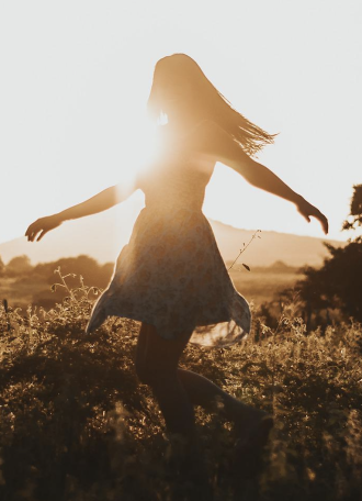 Une femme à contre jour qui danse dans un champ